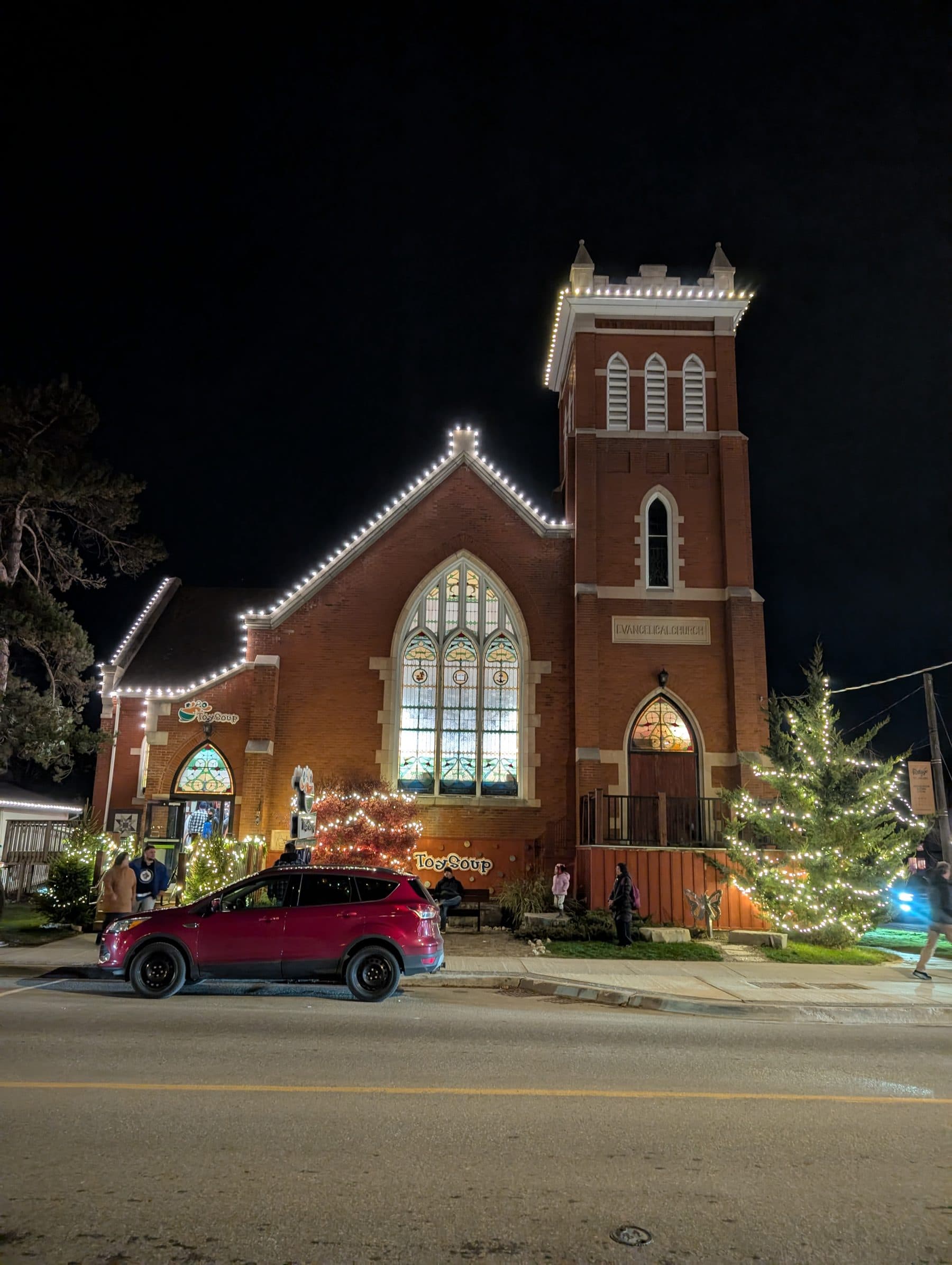 Historic brick church outlined in warm-white roofline lights with wrapped evergreens