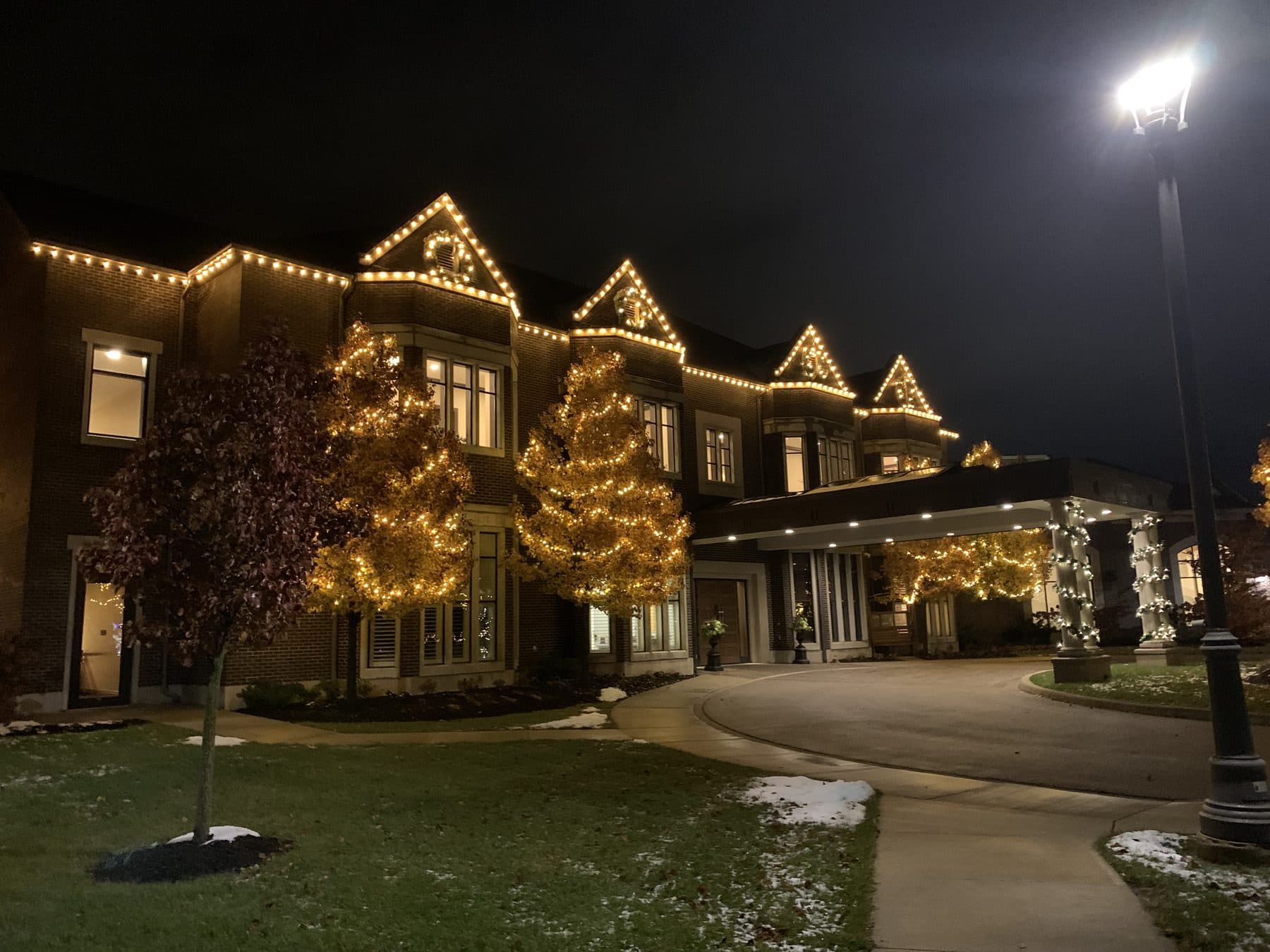 Luxury venue with warm-white roofline lights and mature wrapped trees at night